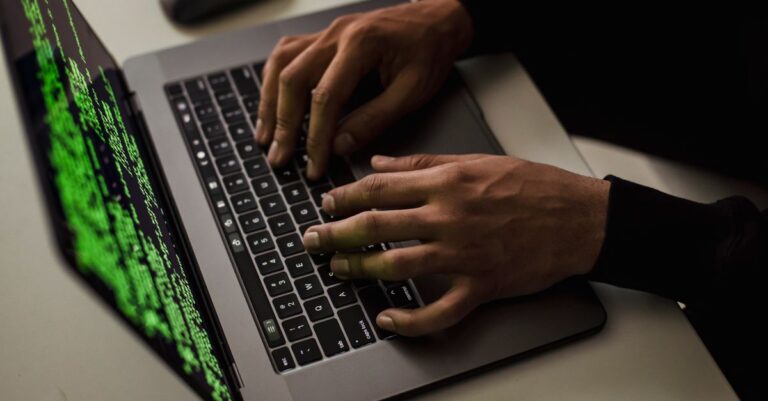 Mani su una tastiera con codice sullo schermo che indica un account violato