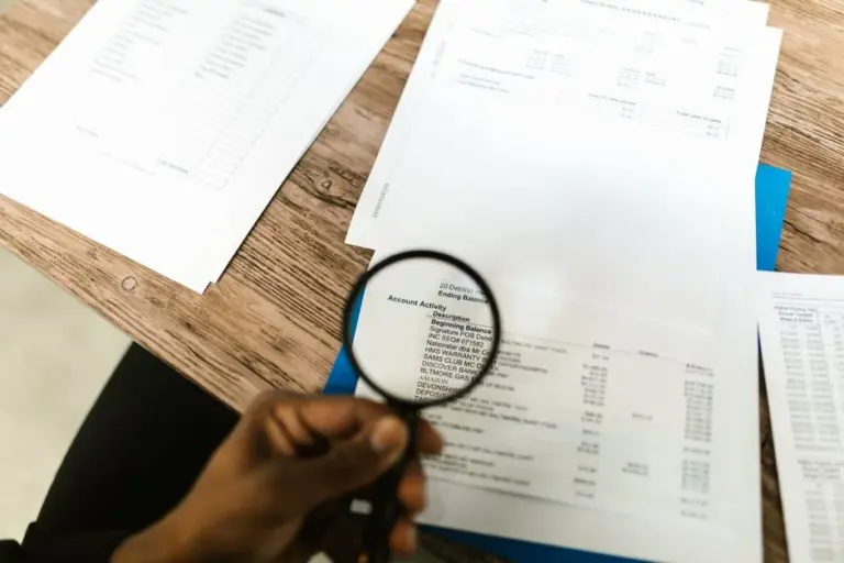Mano che usa una lente d'ingrandimento per esaminare documenti finanziari