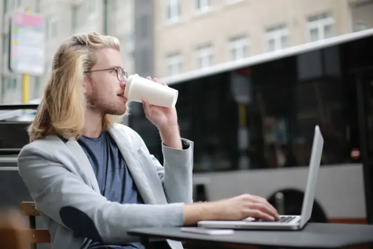 Giovane lavoratore autonomo al computer portatile mentre beve un caffè all'aperto