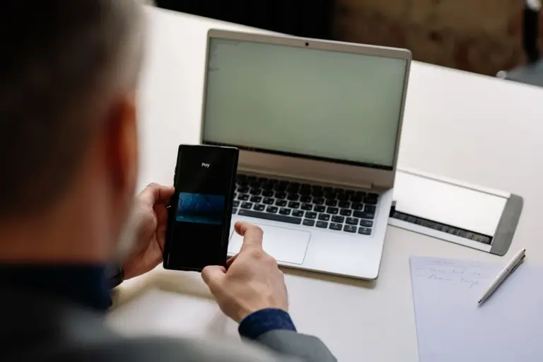 Uomo d'affari che usa il telefono per un pagamento digitale accanto al laptop