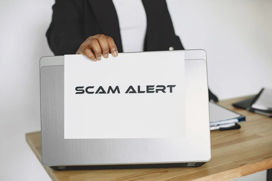 Persona che mostra un cartello di allerta truffa sopra un laptop