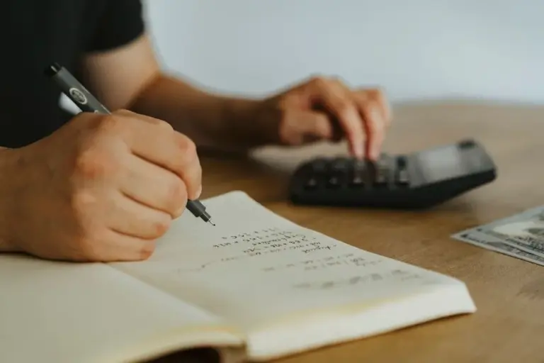 Mani che scrivono calcoli su un quaderno con una calcolatrice