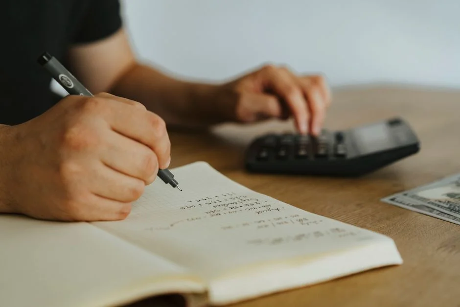 Mani che scrivono calcoli su un quaderno con una calcolatrice