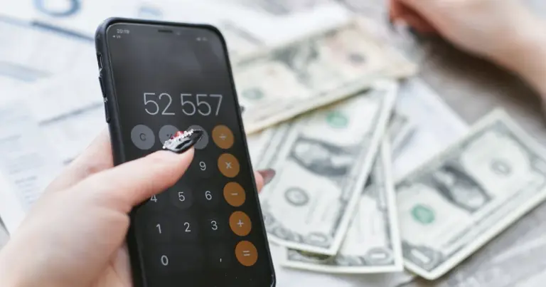 Mani che usano una calcolatrice sullo smartphone accanto a banconote